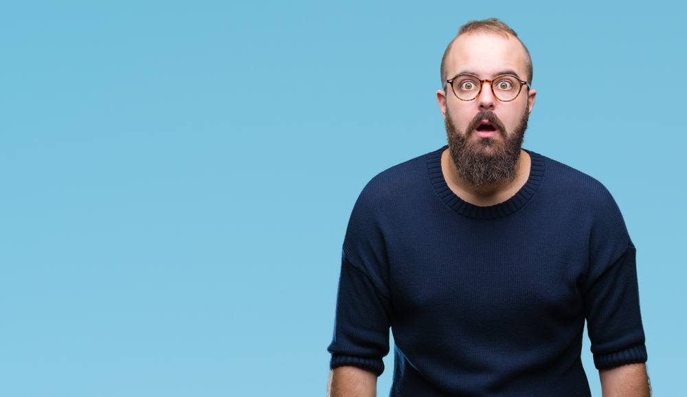 young caucasian hipster man wearing sunglasses over isolated background afraid and shocked with surprise expression, fear and excited face.
